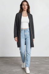 Woman wearing a gray cardigan, white top, light blue jeans, and white sneakers on a plain background