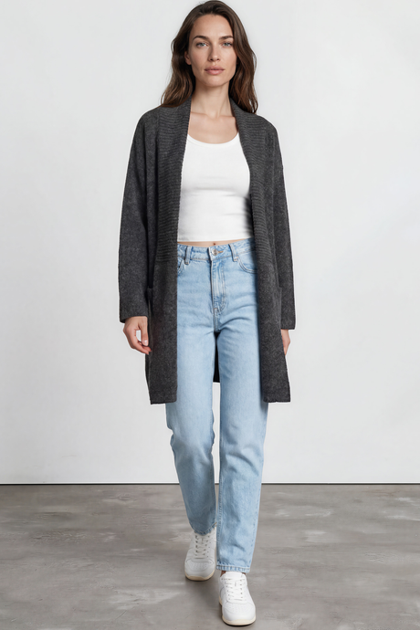 Woman wearing a gray cardigan, white top, light blue jeans, and white sneakers on a plain background