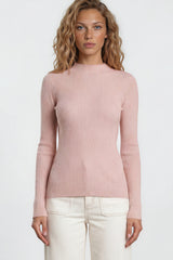 Woman wearing a pink sweater and white pants against a plain background