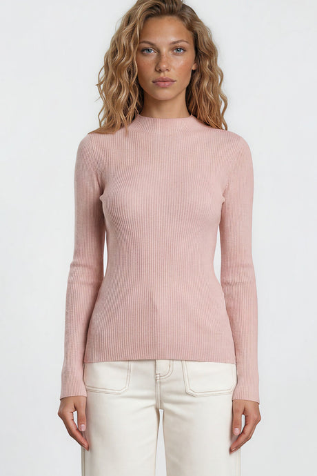 Woman wearing a pink sweater and white pants against a plain background