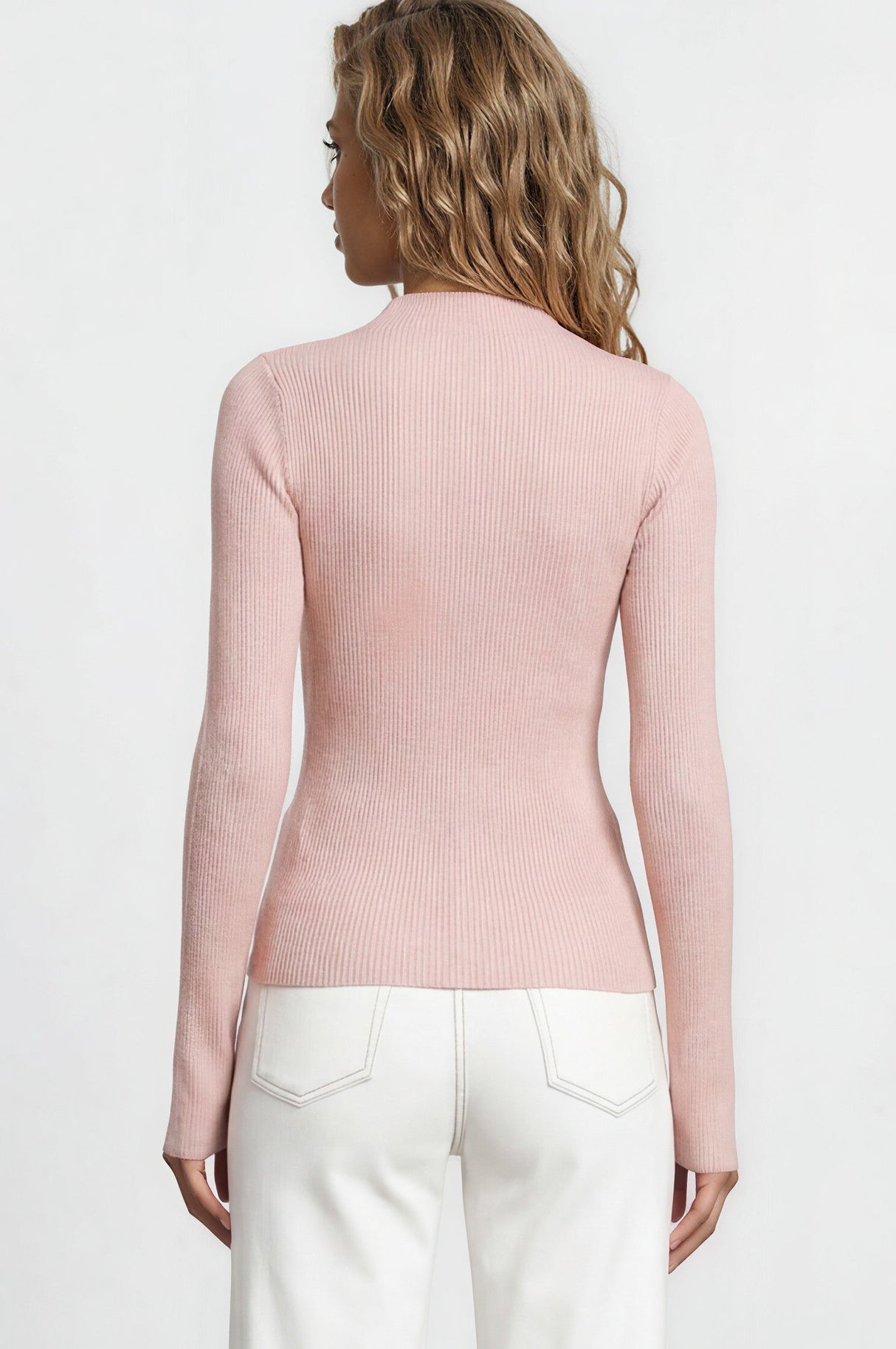 Woman wearing a pink cardigan and white pants against a white background