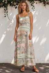 Woman wearing a patterned dress standing against a white wall with greenery.