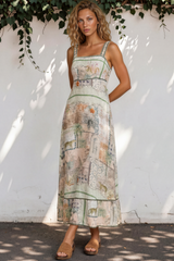 Woman wearing a patterned dress standing against a white wall with greenery.