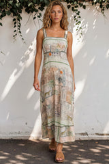 Woman wearing a patterned dress standing against a white wall with greenery.