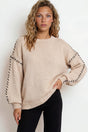 Woman wearing a beige sweater with black trim on a white background