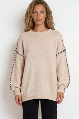 Woman wearing a beige sweater with black and white striped sleeves on a white background