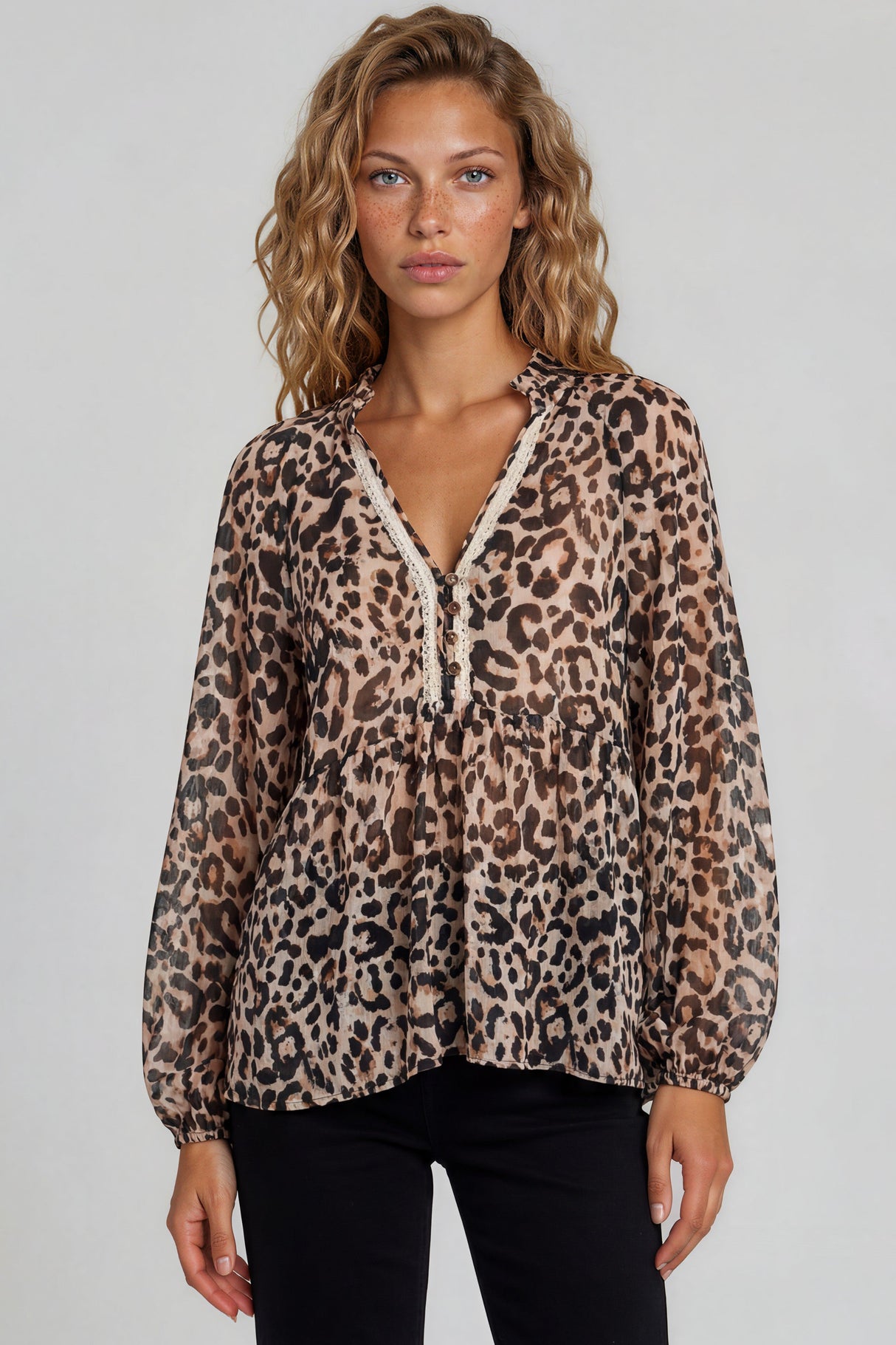 Woman wearing a leopard print blouse with lace trim on a plain background