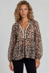 Woman wearing a leopard print blouse with lace trim on a plain background