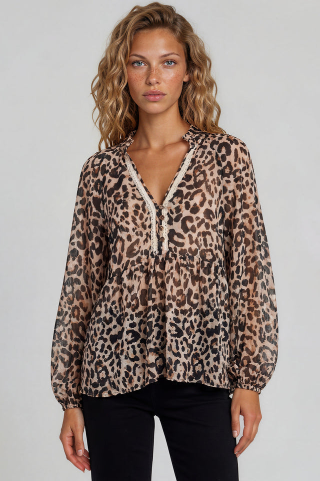 Woman wearing a leopard print blouse with lace trim on a plain background