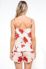Back view of a woman wearing the Soleia Playsuit in Arli Print, a spaghetti strap cami overlay playsuit in a cream and red bold floral print, against a white wall