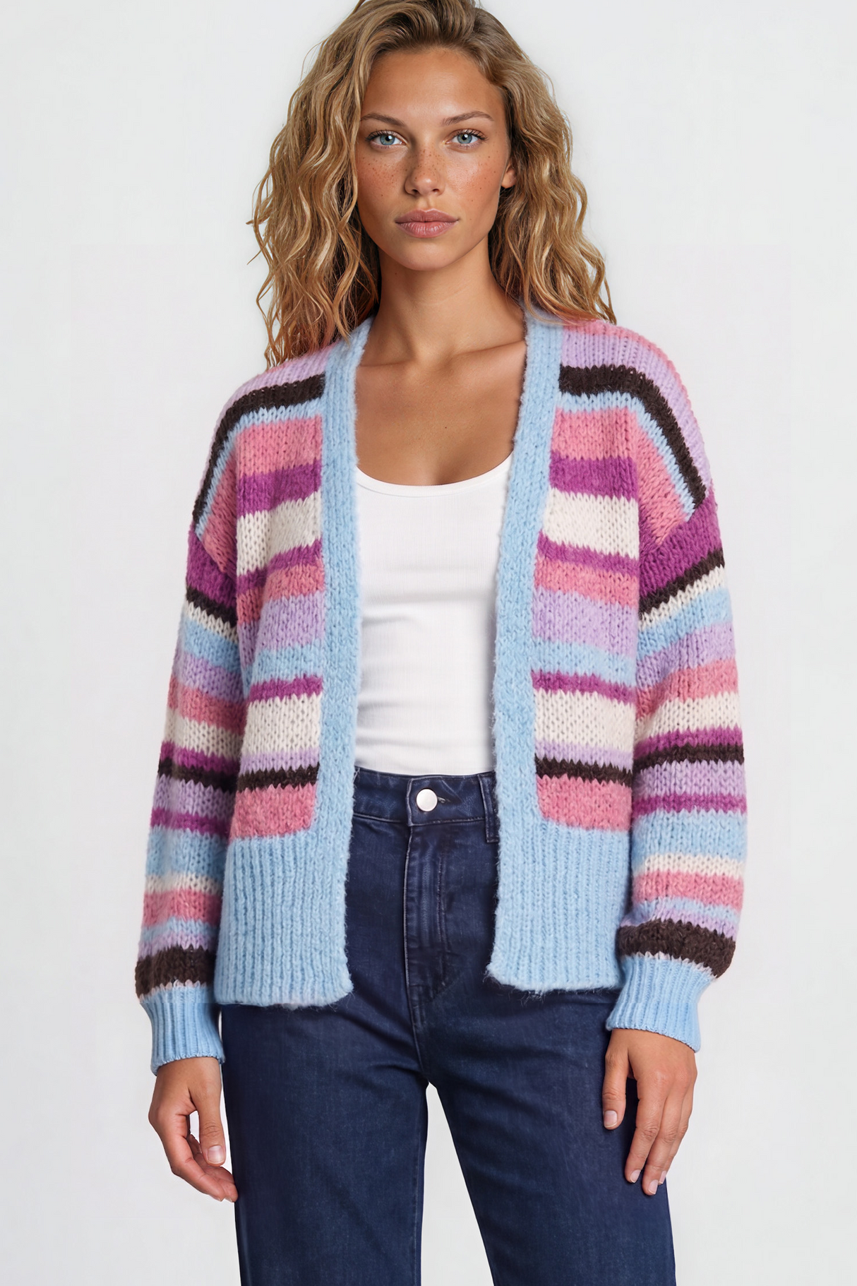 Woman wearing a colorful striped cardigan, white top, and blue jeans on a plain background