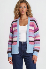 Woman wearing a colorful striped cardigan, white top, and blue jeans on a plain background