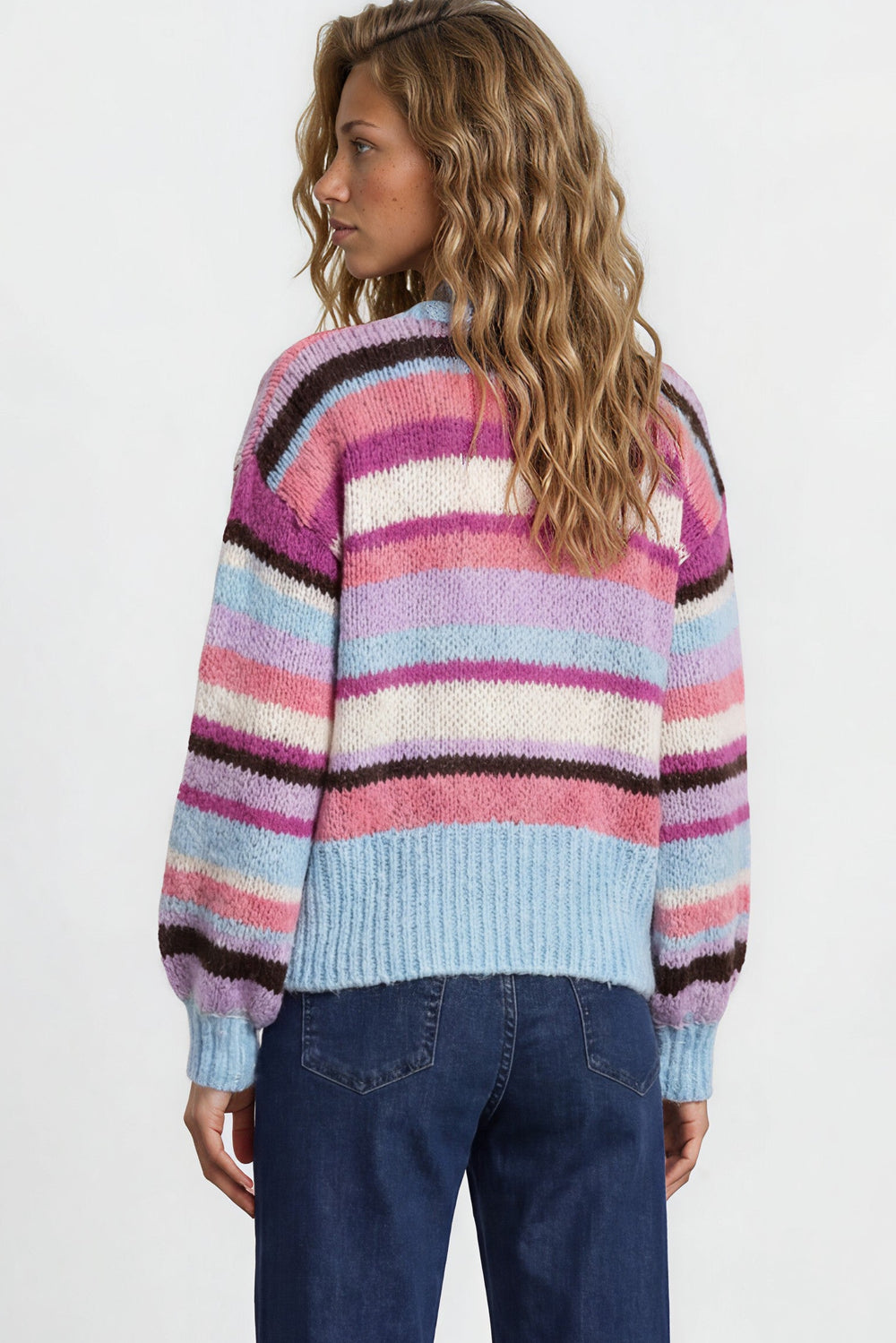 Person wearing a colorful striped sweater and blue jeans on a plain background