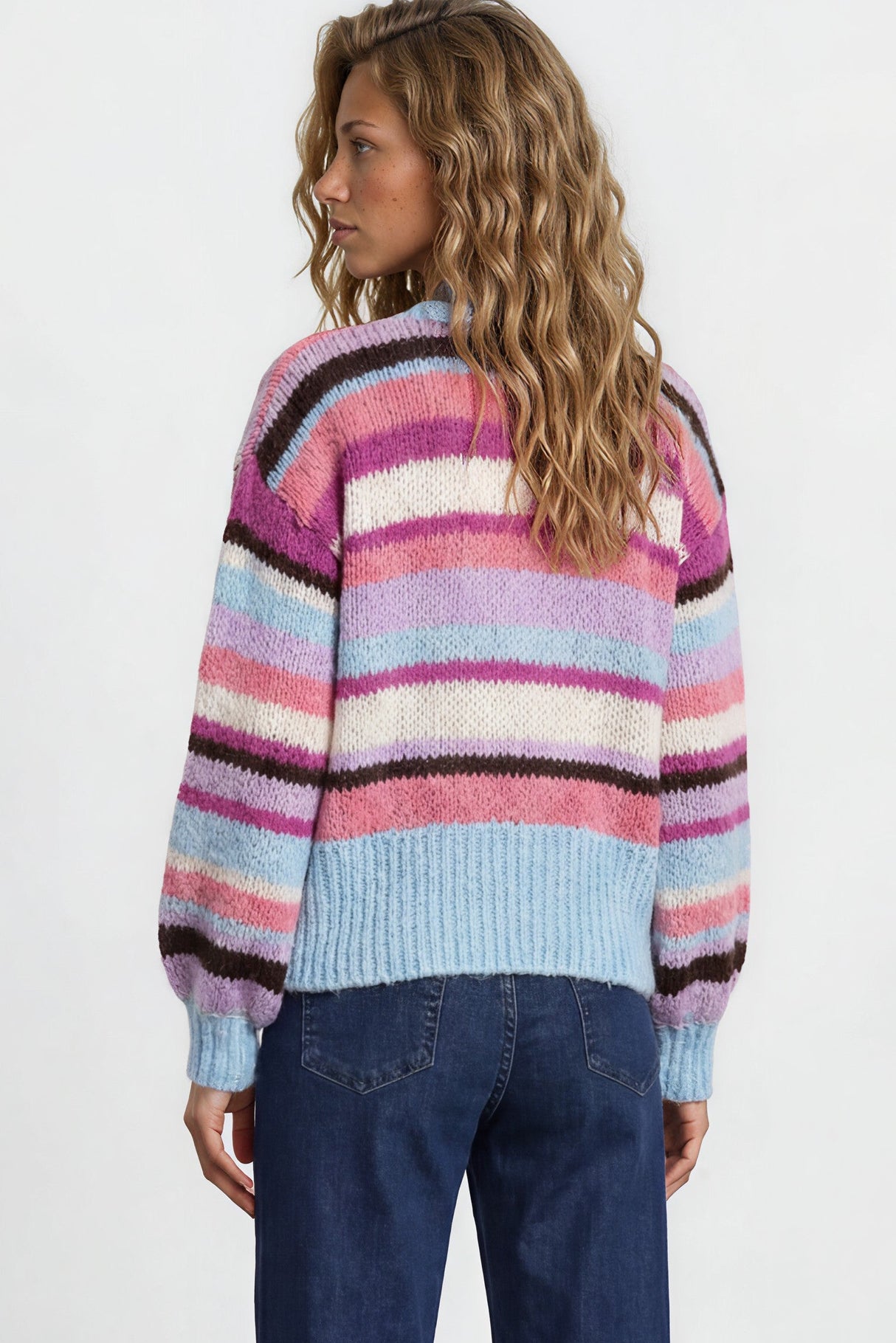 Person wearing a colorful striped sweater and blue jeans on a plain background