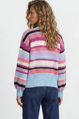 Person wearing a colorful striped sweater and blue jeans on a plain background