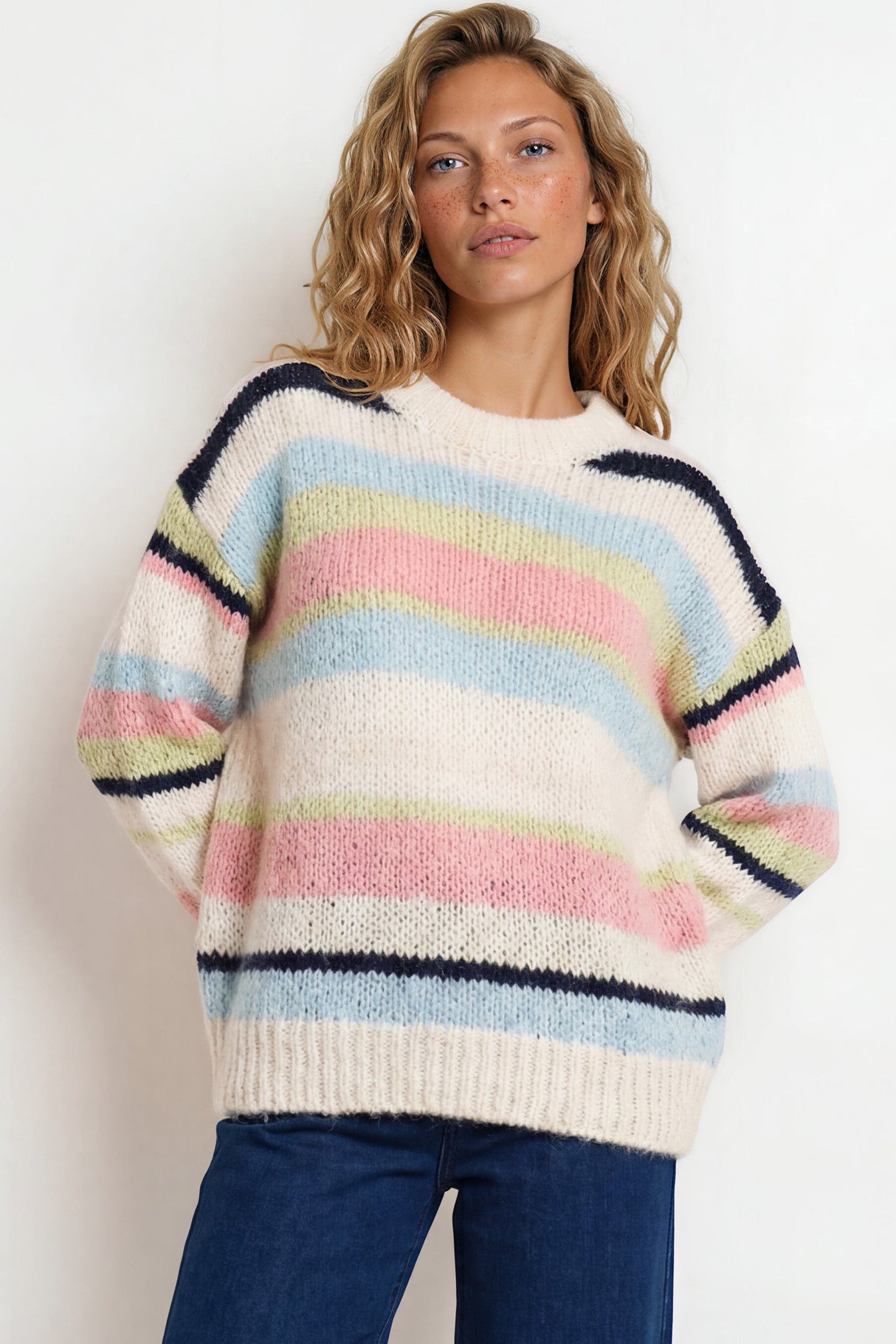 Woman wearing a colorful striped sweater and blue pants against a white background