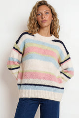 Woman wearing a colorful striped sweater and blue pants against a white background