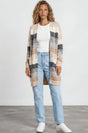 Woman wearing a plaid cardigan, white shirt, blue jeans, and white sneakers on a plain background