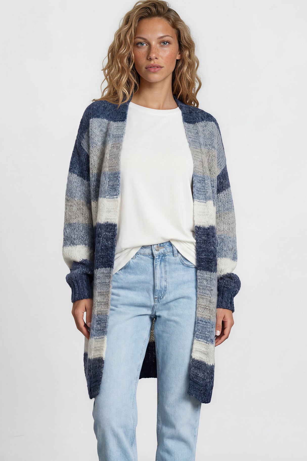 Woman wearing a plaid cardigan, white shirt, light blue jeans, and white sneakers on a plain background