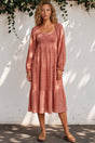 Woman wearing a pink dress standing against a white wall with greenery.