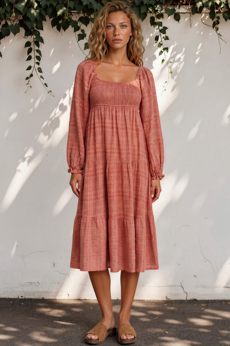 Woman wearing a pink checkered dress standing against a white wall with greenery.