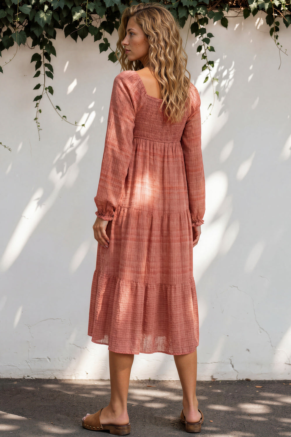 Woman wearing a pink dress standing against a white wall with greenery.