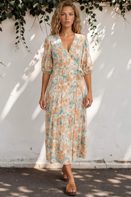 Woman wearing a floral dress standing against a white wall with greenery.
