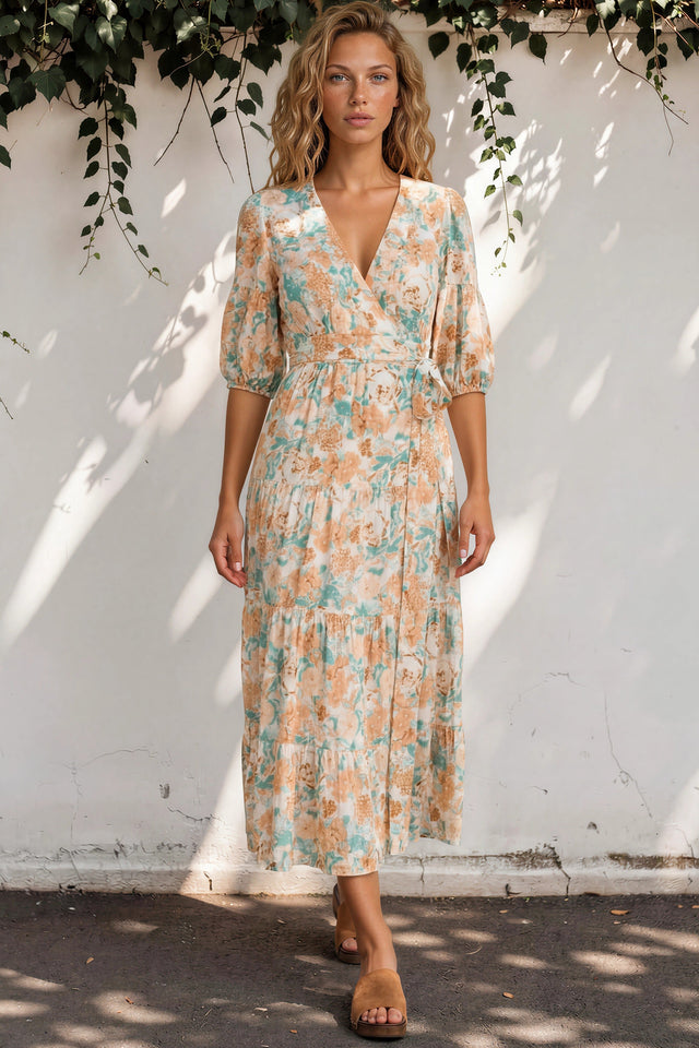 Woman wearing a floral dress standing against a white wall with greenery.