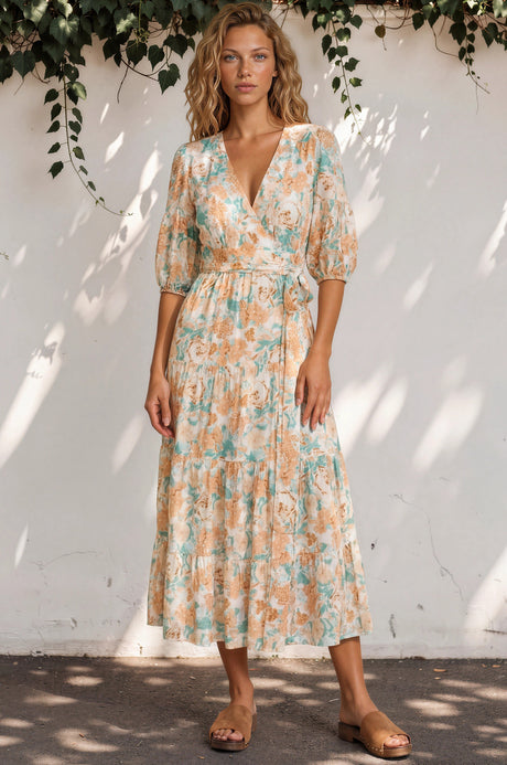 Woman wearing a floral dress standing against a white wall with greenery.