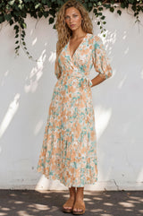 Woman wearing a floral dress against a white wall with greenery.