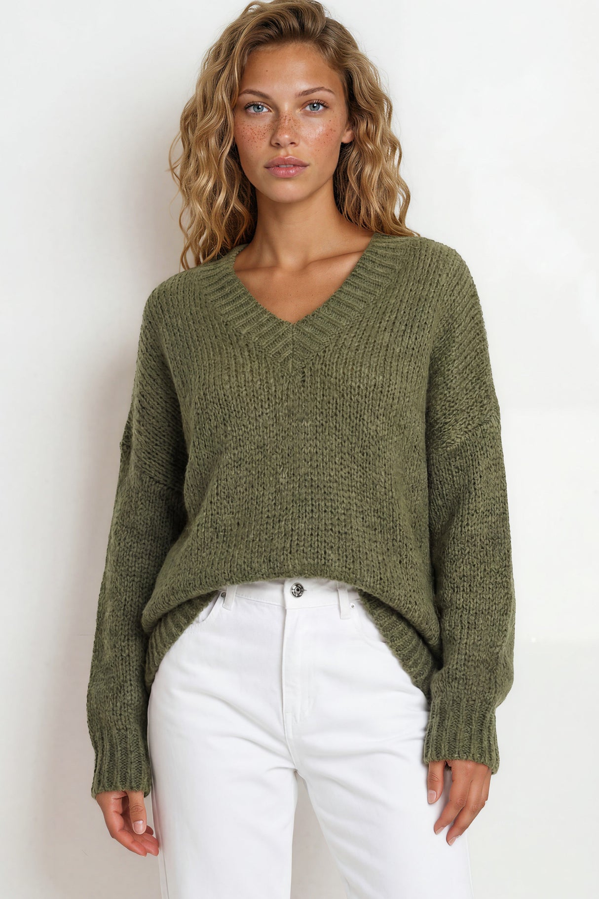 Woman wearing a green sweater and white pants against a white background