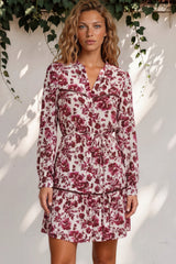 Woman wearing a floral dress standing against a white wall with greenery.