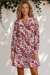 Woman wearing a floral dress standing against a white wall with greenery.
