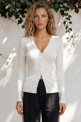 Woman wearing a white cardigan over a black top with a white background and greenery.