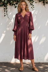 Woman wearing a burgundy dress standing against a white wall with greenery.