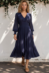 Woman wearing a navy blue dress standing against a white wall with greenery.