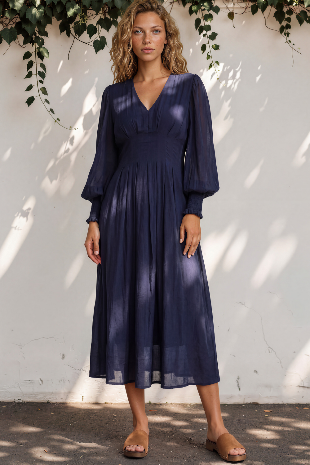 Woman wearing a navy blue dress standing against a white wall with greenery.