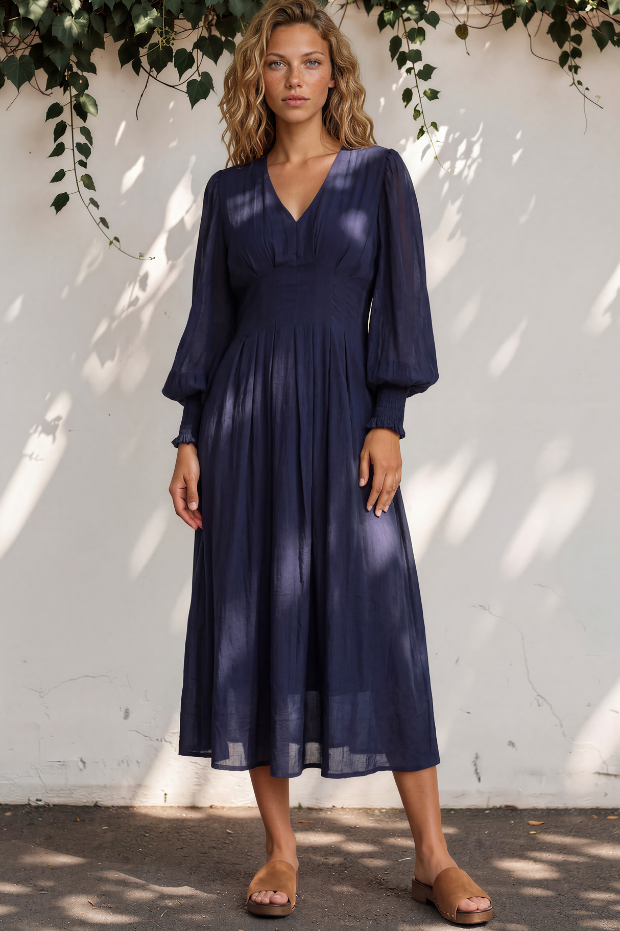 Woman wearing a navy blue dress standing against a white wall with greenery.