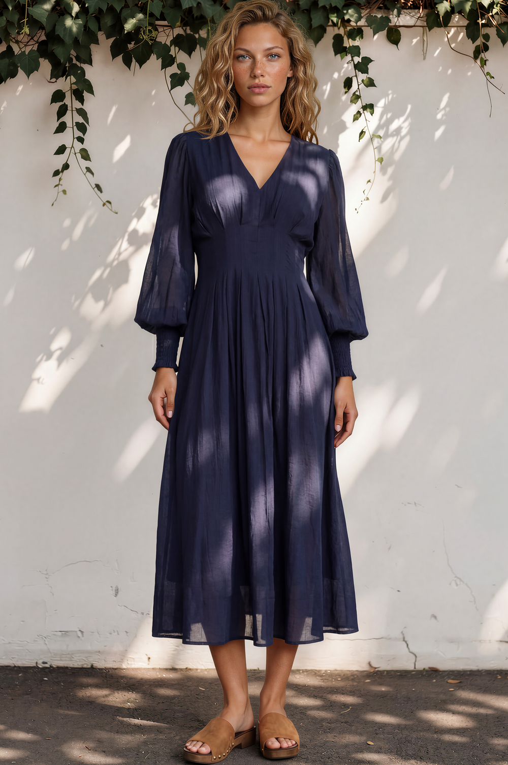 Woman wearing a navy blue dress standing against a white wall with greenery.