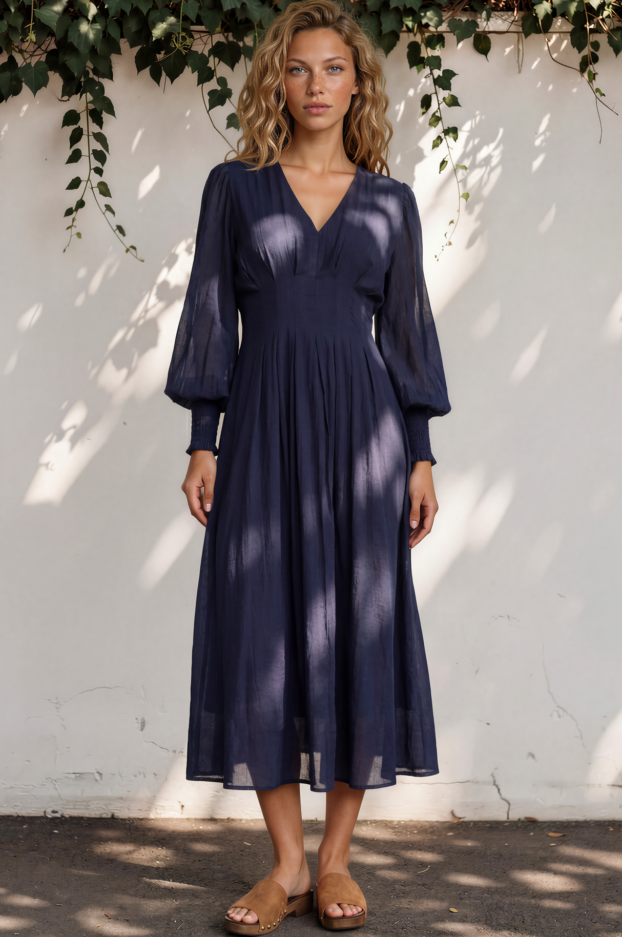 Woman wearing a navy blue dress standing against a white wall with greenery.