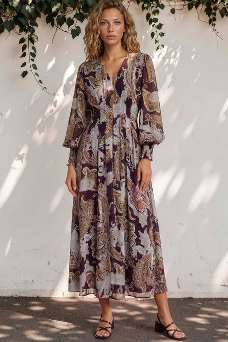 Woman wearing a patterned dress standing against a white wall with greenery.