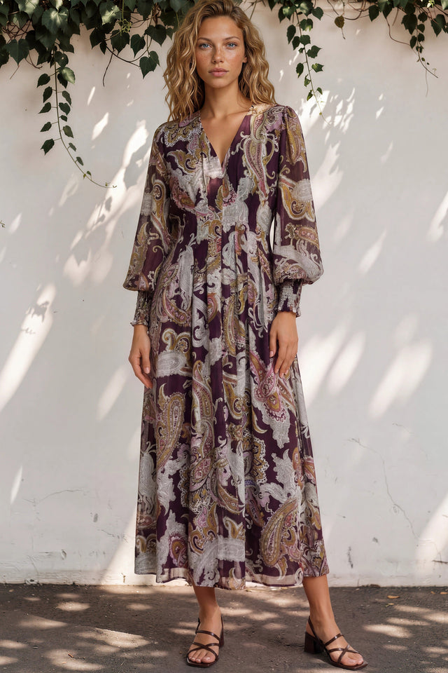 Woman wearing a patterned dress standing against a white wall with greenery.
