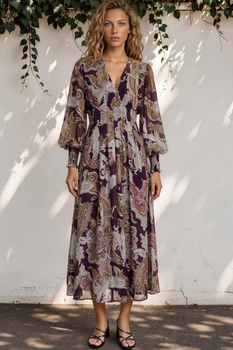 Woman wearing a patterned dress standing against a white wall with greenery.