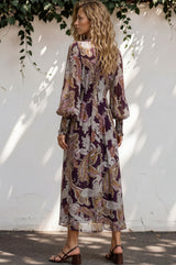 Woman wearing a patterned dress standing against a white wall with greenery.