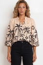 Woman wearing a blouse with palm tree pattern against a plain background