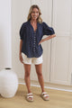 A woman in a relaxed navy blouse with voluminous puff sleeves and a split tie neckline, posed in front of a beige closet.